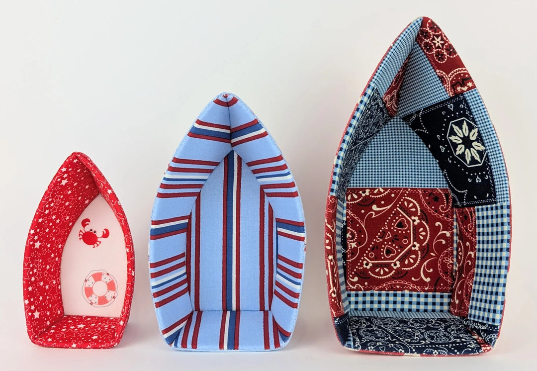 Three fabric bowls shaped like boats in varying sizes featuring patchwork designs and patterns, showcasing the English Paper Piecing Bowls Pattern - The Dory Boat.