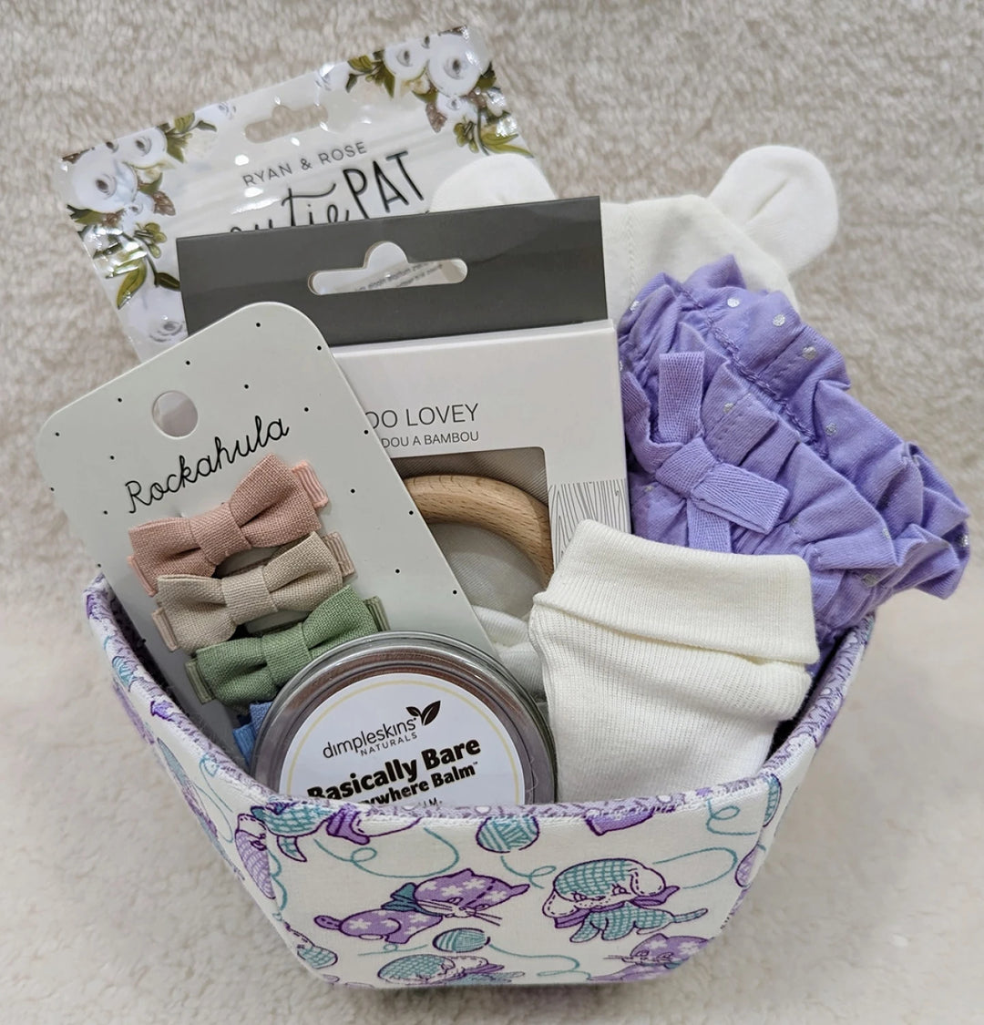 Fabric basket with a pastel pattern holding baby care items including socks, hair bows, balm, and a teething ring, showcasing the English Paper Piecing Bowls Pattern - The Goodness Bowl design.