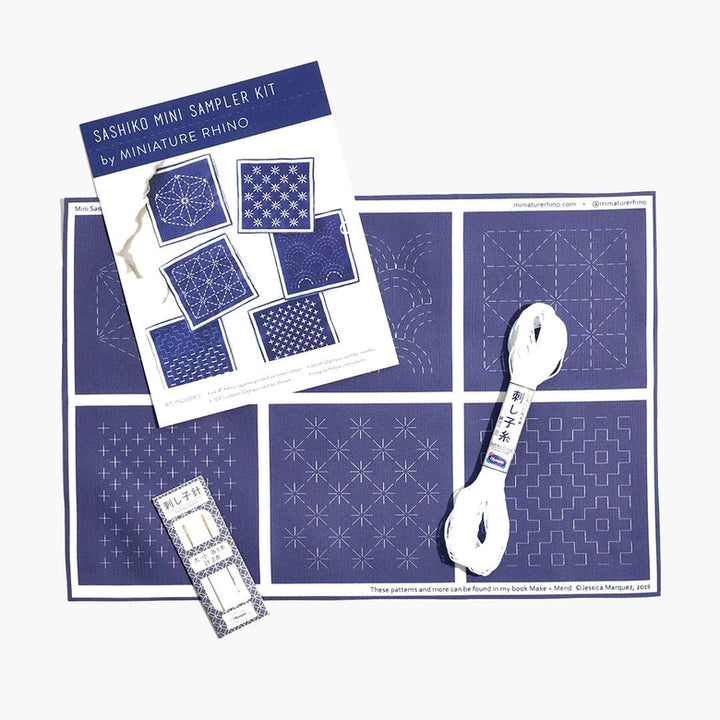 Sashiko Mini Sampler Kit (No. 1) featuring blue fabric with white printed Sashiko patterns, white embroidery floss, needles, and a pattern guide for modern needlework and Japanese craft supplies.