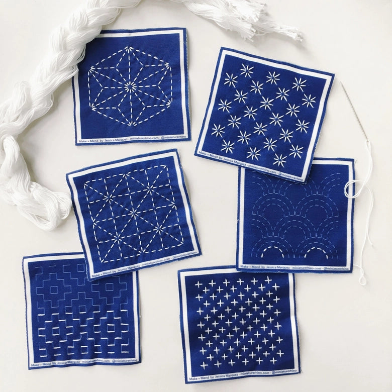 Sashiko Mini Sampler Kit (No. 1) featuring six blue fabric squares with traditional white Sashiko embroidery patterns, embroidery floss, and needle for modern needlework craft enthusiasts.