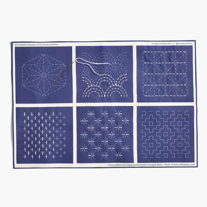 Sashiko Mini Sampler Kit (No. 1) featuring six traditional white sashiko stitching patterns on indigo fabric, including a threaded needle for practicing Japanese needlework techniques.