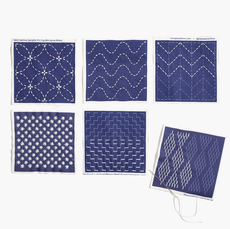 Collection of six small navy blue fabric pieces showcasing different white sashiko embroidery patterns with needle and white thread, part of the Sashiko Mini Sampler Kit (No. 2)