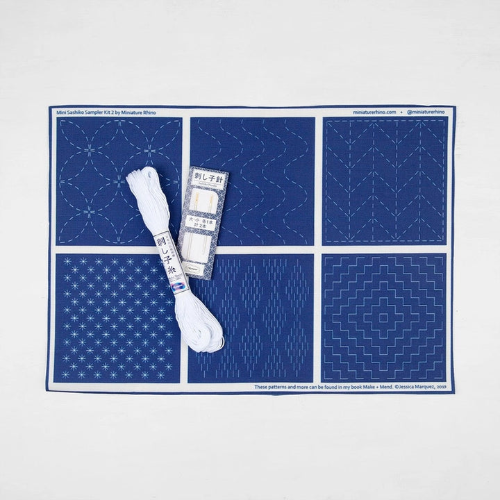 Sashiko Mini Sampler Kit (No. 2) featuring blue fabric with traditional white Sashiko embroidery patterns, including embroidery thread and needles for Japanese craft supplies.