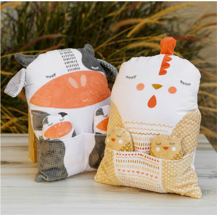 Soft fabric animal pillows featuring a cow and chicken with small matching baby animals in front pockets, designed as the Farmstead Cuddle Animal Pillow Panel for cozy home decor and crafting.
