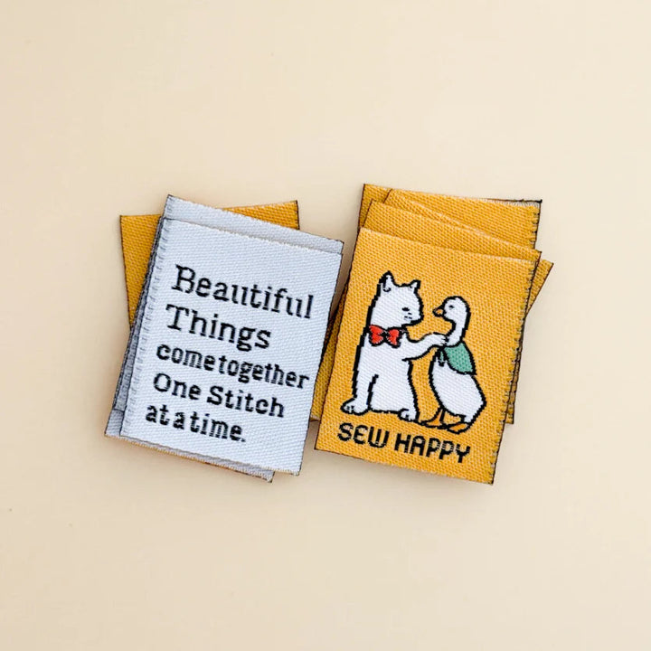 Two yellow woven labels with embroidered designs on a beige background
