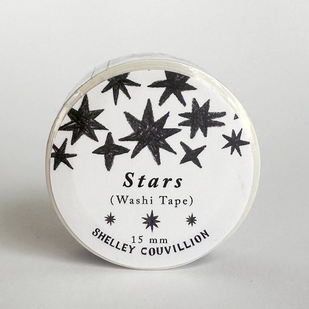 A roll of white washi tape with black glittery star patterns, labeled 'Stars (Washi Tape) 15 mm SHELLEY COUVILLION', on a light gray background.