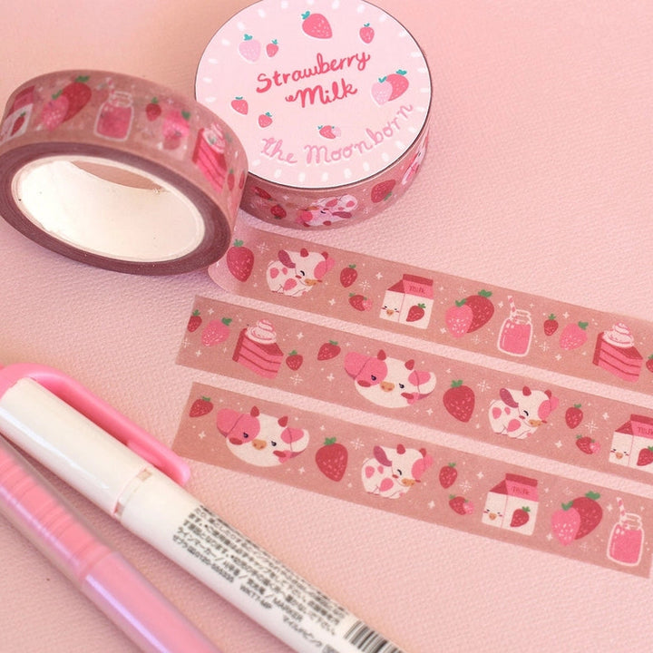 Pink washi tape with strawberry and dessert illustrations, shown with two rolls and several strips on a pink background, alongside a pink pen and a white marker.