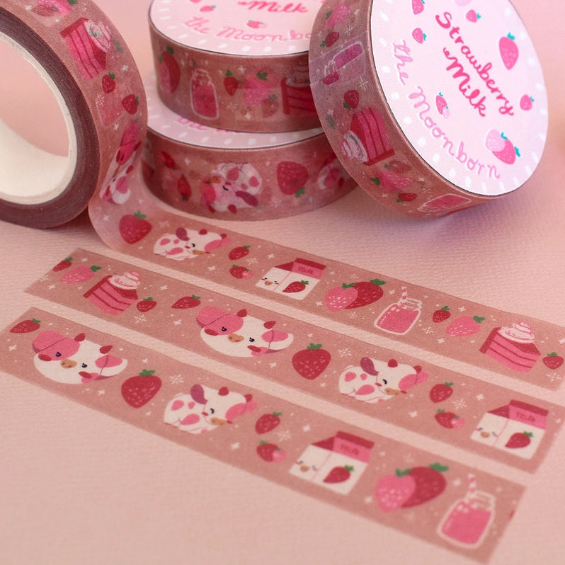 Pink washi tape with a strawberry and cat pattern, shown in rolls and strips on a pink background, alongside pink pens and a clear bottle.