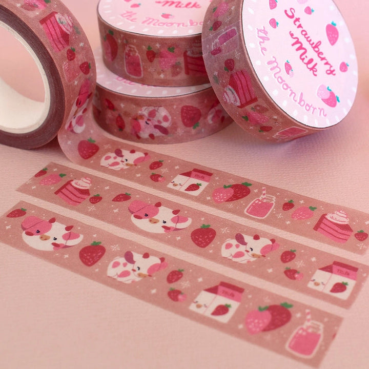 Pink washi tape with a strawberry and cat pattern, shown in rolls and strips on a pink background, alongside pink pens and a clear bottle.