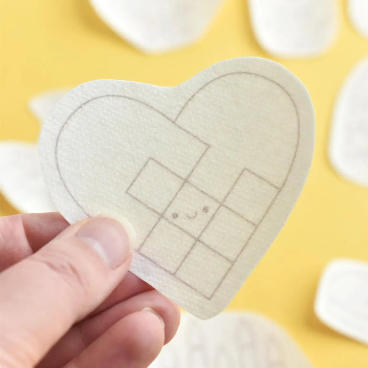 Heart-shaped adhesive patch held by a hand on a yellow background