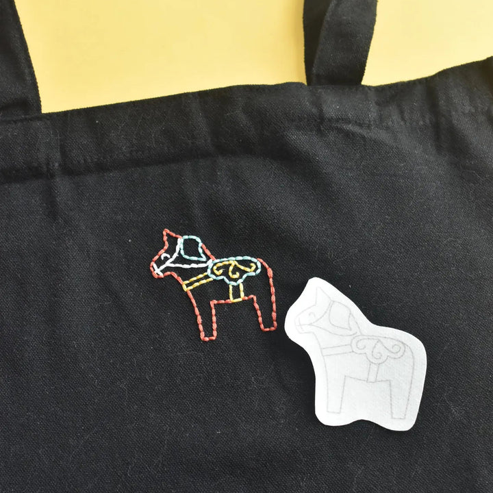 Black apron with embroidered horse design and white star patch on a yellow background