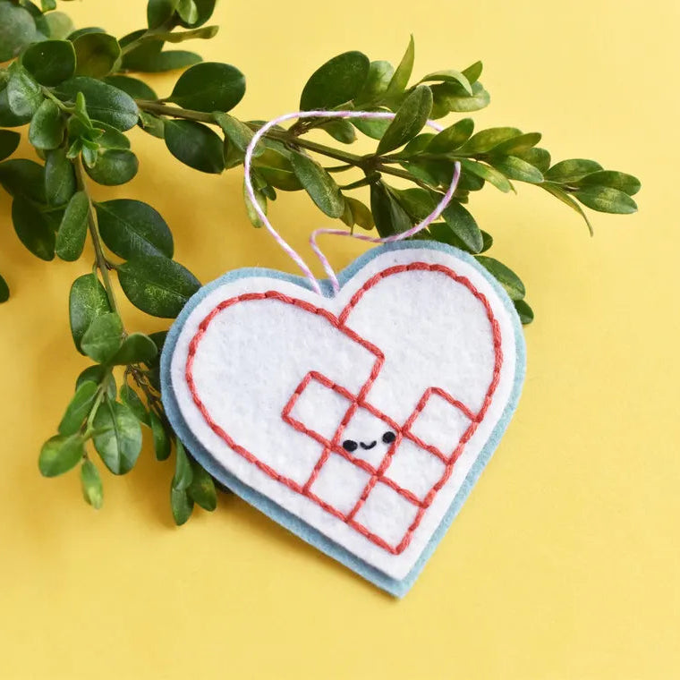 Heart-shaped embroidered ornament with a grid pattern on a yellow background