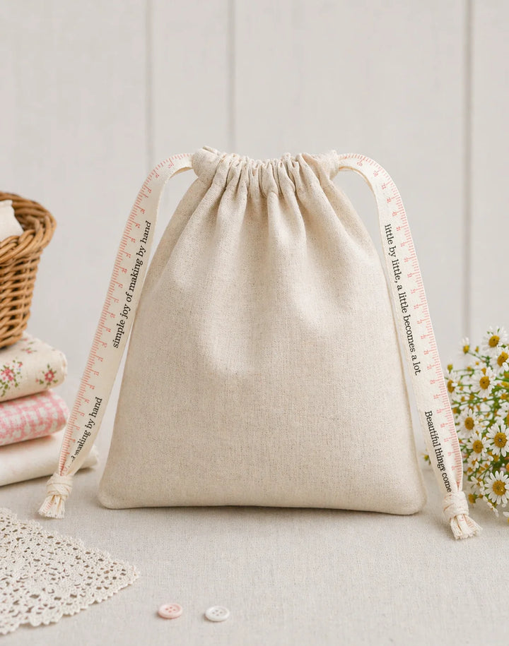 Beige drawstring bag with printed strings on a light wooden surface.