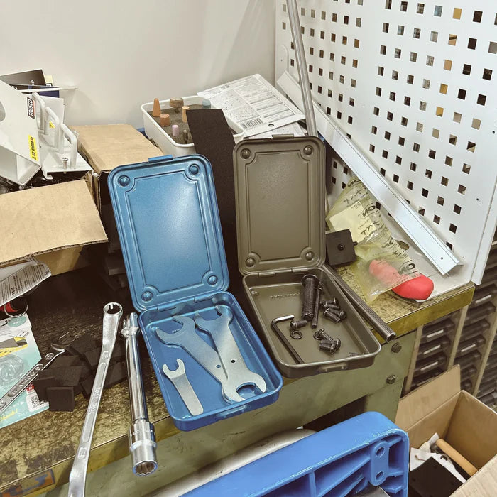 Toyo Steel T-152 Small Metal Storage Box in blue and green, open to display tools inside, placed on a cluttered workbench with various hardware and craft supplies around.