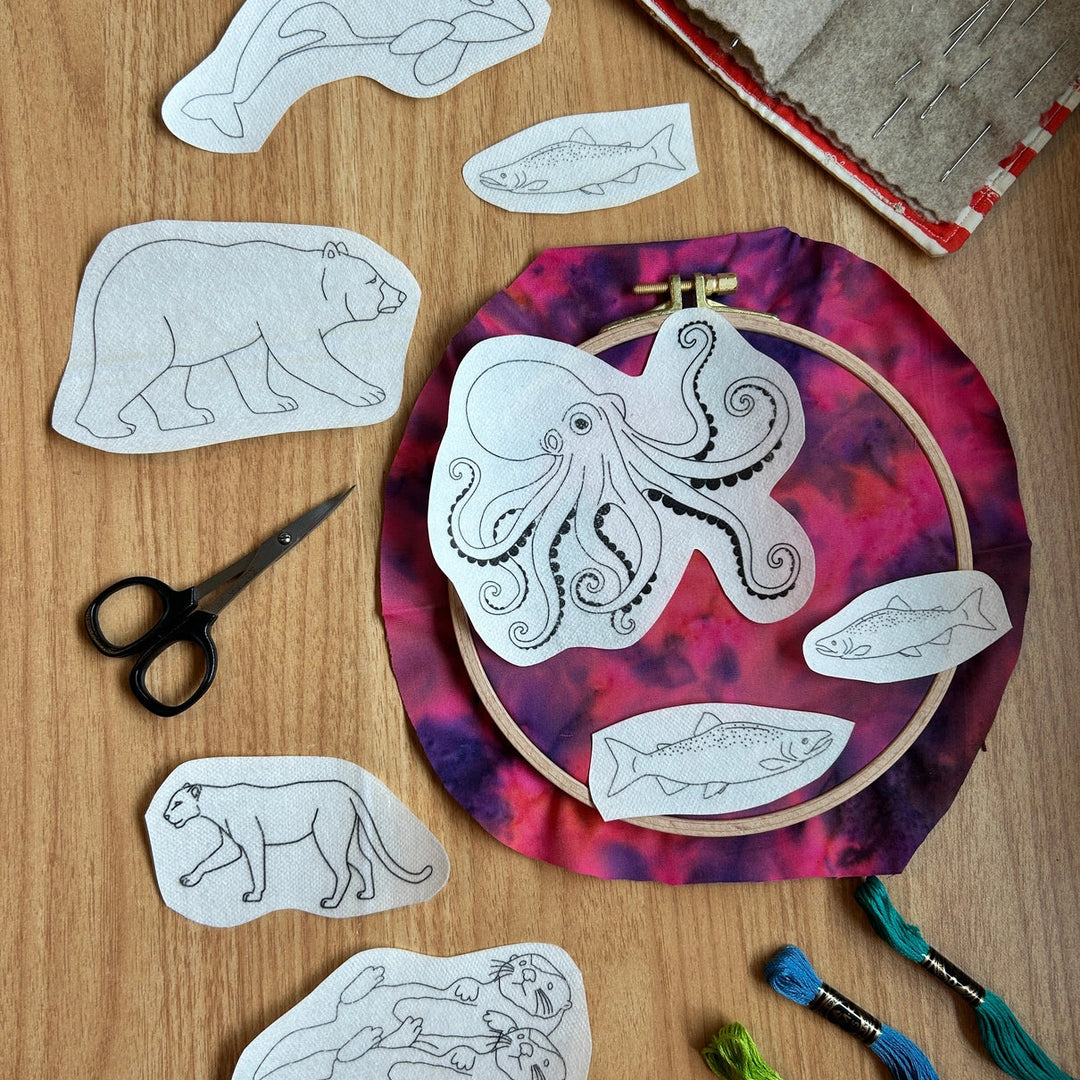 Embroidery hoop with octopus design and fabric pieces on a wooden surface