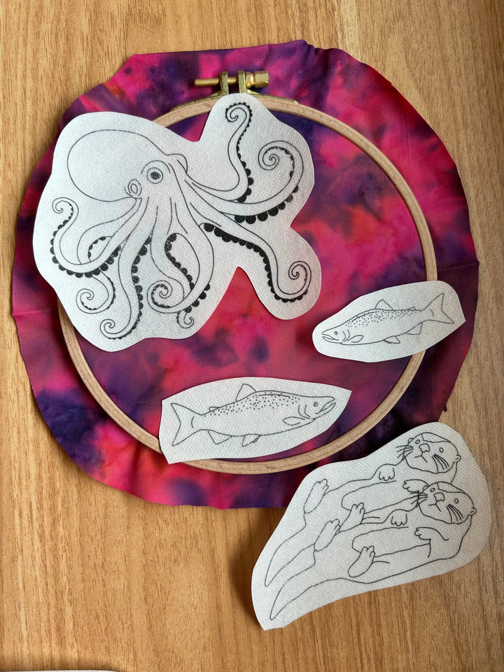 PNW Animals Stick & Stitch Embroidery Patterns featuring outlined designs of an octopus, two fish, and two otters on fabric stretched in an embroidery hoop for modern needlework.