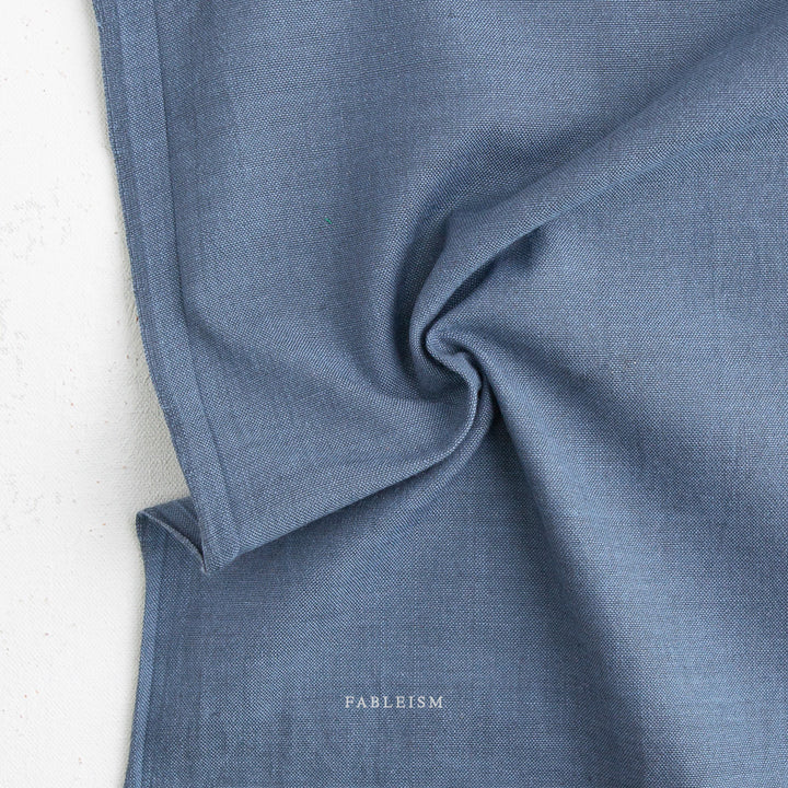 Close-up of a soft textured blue fabric with subtle watercolor shading, showcasing Watercolor Wovens Shot Cotton - French Blue (FWW300) ideal for quilting and modern needlework projects.