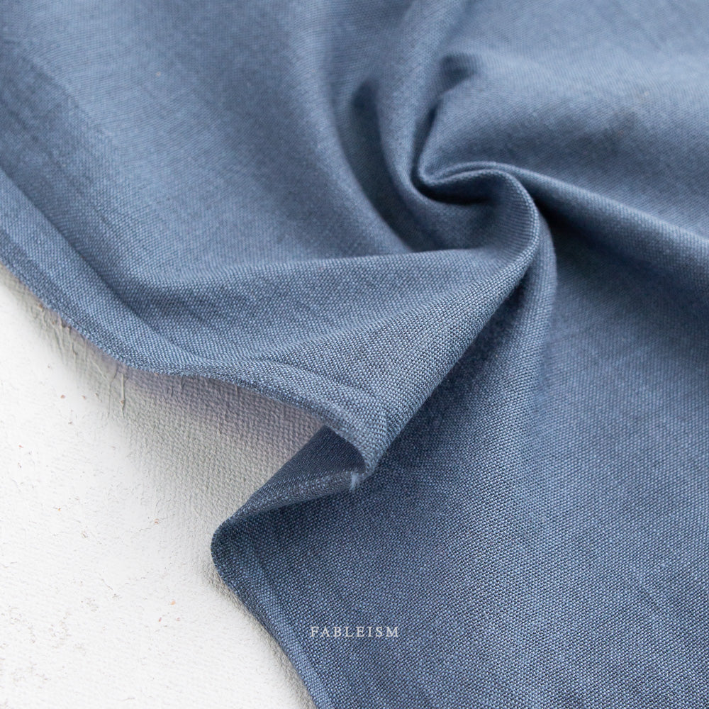 Close-up of soft textured fabric in muted blue tone, showcasing Watercolor Wovens Shot Cotton - French Blue (FWW300) ideal for modern needlework, embroidery, and quilting projects.